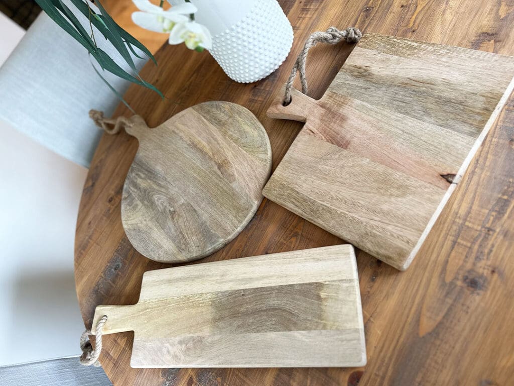 Set of handcrafted wooden serving boards with rustic rope handles, displayed on a wooden dining table.